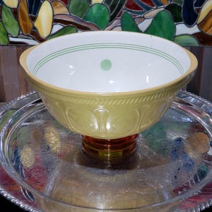May include: A yellow ceramic mixing bowl with a white interior featuring thin green circular lines and a single green dot. The exterior has a textured rope pattern near the rim and a repeating embossed geometric design around the lower body.