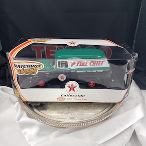 May include: A Matchbox Collectibles 1957 GMC Panel Van toy in its original packaging. The van is black and green with red wheels and Texaco branding. The words "FIRE CHIEF" and "SERVICE YOU CAN TRUST" are visible on the side.