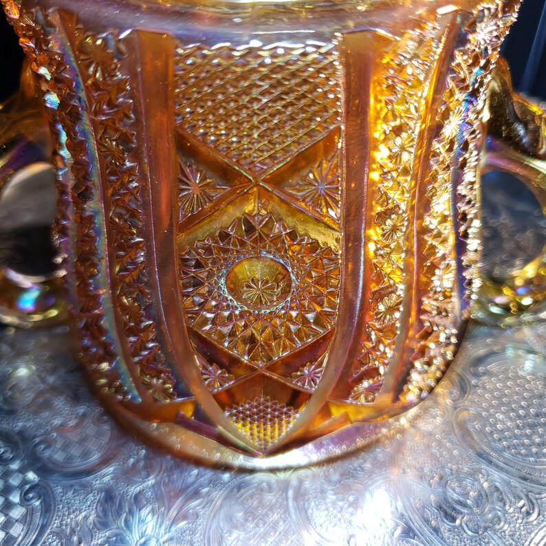 May include: A vintage amber glass bowl with a detailed geometric pattern. The bowl has a scalloped edge and two handles.