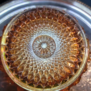 May include: A close-up of a vintage amber glass plate with a diamond pattern. The center of the plate has a smaller, circular design with a starburst pattern.