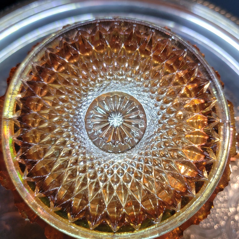 May include: A close-up of a vintage amber glass plate with a diamond pattern. The center of the plate has a smaller, circular design with a starburst pattern.