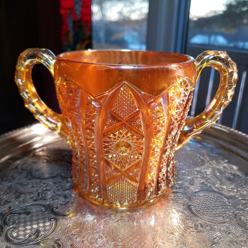May include: A vintage amber glass pitcher with a diamond pattern and two handles. The pitcher is sitting on a silver tray.