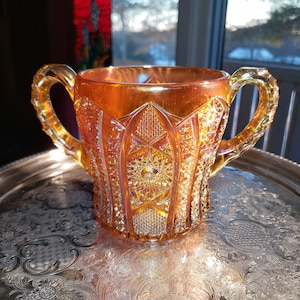 May include: A vintage amber glass pitcher with a diamond pattern and two handles. The pitcher is sitting on a silver tray.