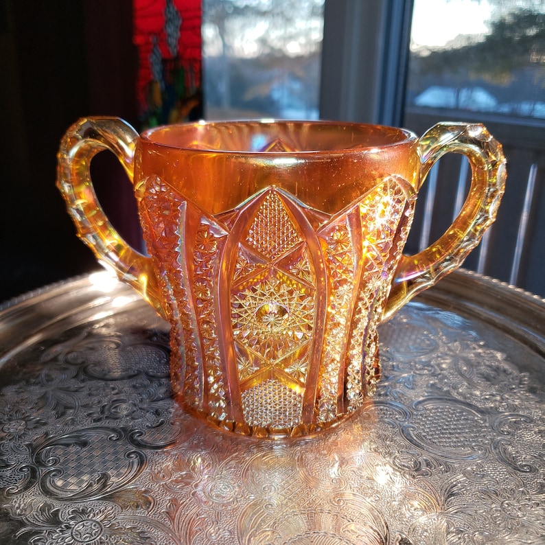 May include: A vintage amber glass pitcher with a diamond pattern and two handles. The pitcher is sitting on a silver tray.