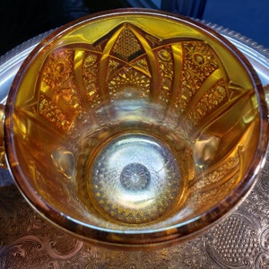 May include: A vintage amber glass bowl with a decorative, geometric pattern. The bowl has a wide rim and a deep, round interior.