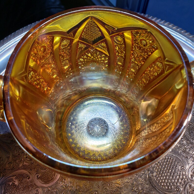 May include: A vintage amber glass bowl with a decorative, geometric pattern. The bowl has a wide rim and a deep, round interior.
