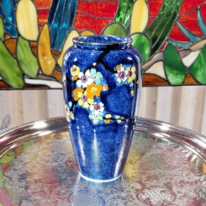 May include: A blue ceramic vase with a gold rim and a floral design. The vase is decorated with white, yellow, orange, and pink flowers on a dark blue background.