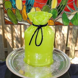 May include: A lime green glass vase shaped like a bag with a black ribbon tie. The vase is sitting on a silver tray.