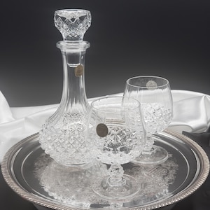 Peut inclure: Un ensemble de trois carafes et verres en verre transparent avec un motif en diamant. La carafe a un bouchon et les verres ont un large bol et une tige.