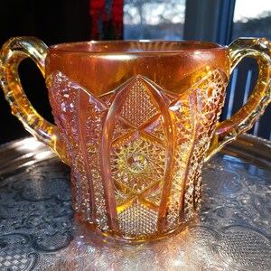 May include: A vintage amber glass pitcher with a diamond pattern and iridescent finish. The pitcher has two handles and a wide mouth.
