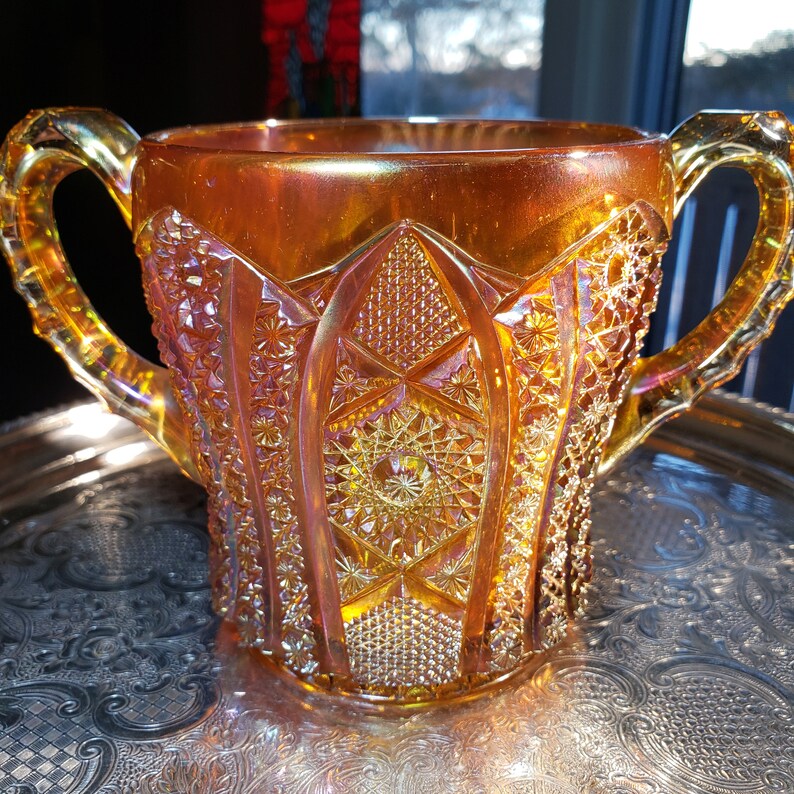 May include: A vintage amber glass pitcher with a diamond pattern and iridescent finish. The pitcher has two handles and a wide mouth.