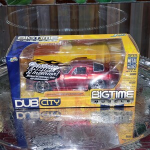May include: A red 1963 Chevy Corvette Sting Ray die-cast model car in a Bigtime Muscle Dub City box. The packaging features yellow and blue accents with text including Custom Engine & Interior and 1:24 scale metal vehicle information.