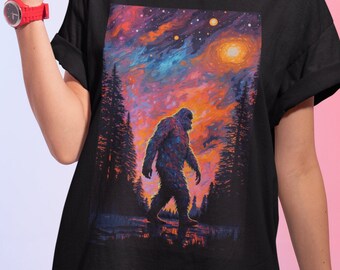 May include: Black t-shirt with a colorful graphic print of a Bigfoot walking through a forest under a starry sky.