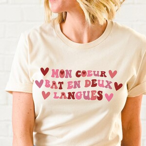 May include: A white t-shirt with a pink and red graphic that says "Mon coeur bat en deux langues" with hearts around the text.