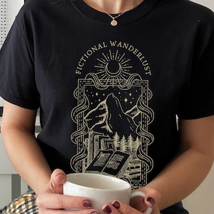 K&ouml;nnte beinhalten: Schwarzes T-Shirt mit einem goldenen Grafikdesign, das eine Bergkette, einen Halbmond und Sterne zeigt. Der Text "Fictional Wanderer" ist in einem Kreis um die Grafik geschrieben.