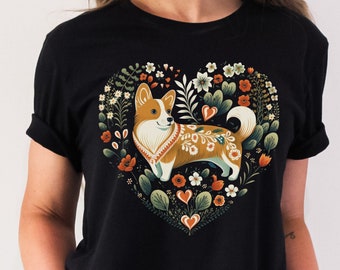 May include: Black t-shirt with a heart-shaped design featuring a corgi dog surrounded by flowers and leaves. The corgi is wearing a floral patterned collar.