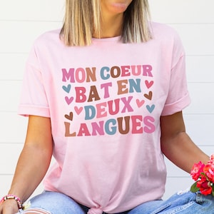 May include: A pink t-shirt with the text "MON COEUR BAT EN DEUX LANGUES" in colorful letters with hearts around the words.