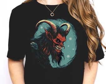 Puede incluir: Camiseta negra con un gráfico de una criatura roja con cuernos y barba, sobre un fondo azul con copos de nieve.
