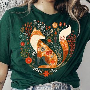 May include: A green t-shirt with a colorful fox illustration surrounded by flowers. The fox is orange, white, and brown with floral patterns. The flowers are red, orange, yellow, and green.