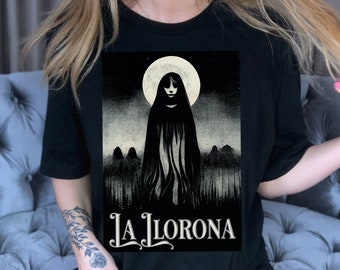May include: A black t-shirt with a graphic print of a woman in a white gown standing in front of a full moon. The text "La Llorona" is printed below the graphic.
