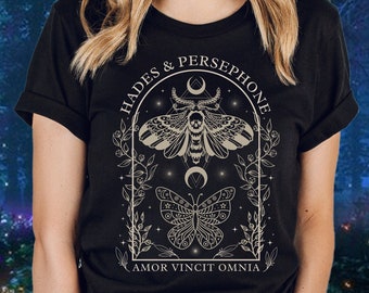 May include: Black t-shirt with a graphic design featuring a moth and butterfly with the text "Hades & Persephone" and "Amor Vincit Omnia".