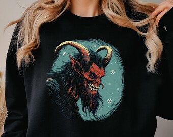 Könnte beinhalten: Schwarzer Pullover mit einem Grafikdruck eines roten, gehörnten Wesens mit Bart vor einem blauen Hintergrund mit Schneeflocken.