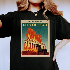 May include: Black t-shirt with a vintage travel poster design featuring a burning building and a horse. The poster reads "visit the beautiful CITY OF TROY".