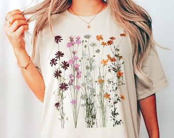 May include: A beige oversized t-shirt with a floral print featuring a variety of flowers in shades of pink, purple, orange, and white.