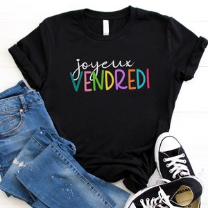 May include: Black t-shirt with the text "Joyeux Vendredi" in colorful letters. The shirt is paired with blue jeans and white sneakers.