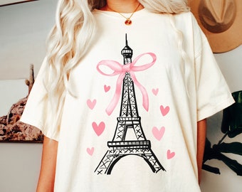 May include: A white t-shirt with a black and white illustration of the Eiffel Tower with a pink bow and pink hearts.