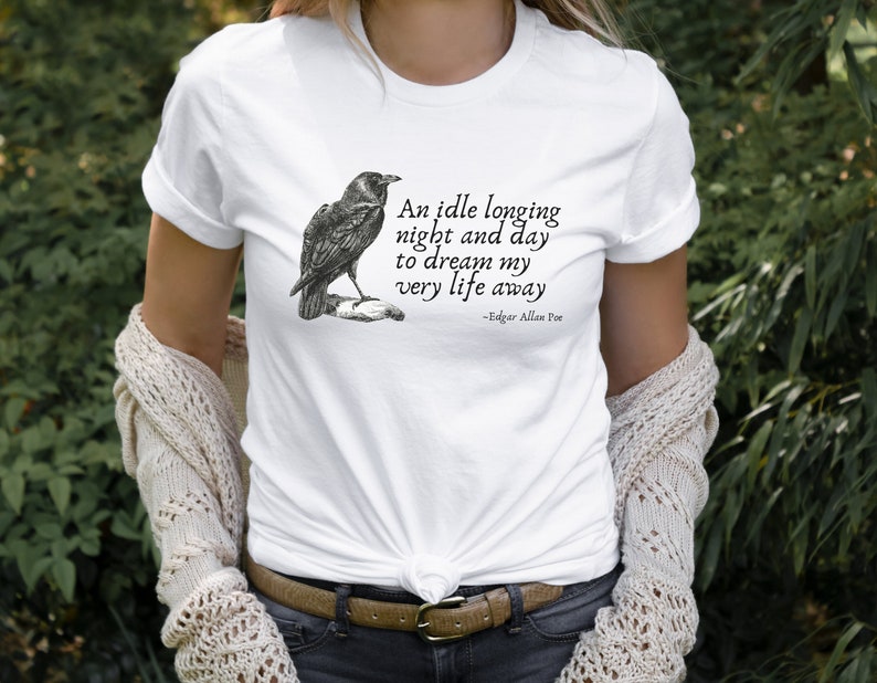 May include: White t-shirt featuring a black and white illustration of a raven and a quote by Edgar Allan Poe: "An idle longing night and day to dream my very life away".
