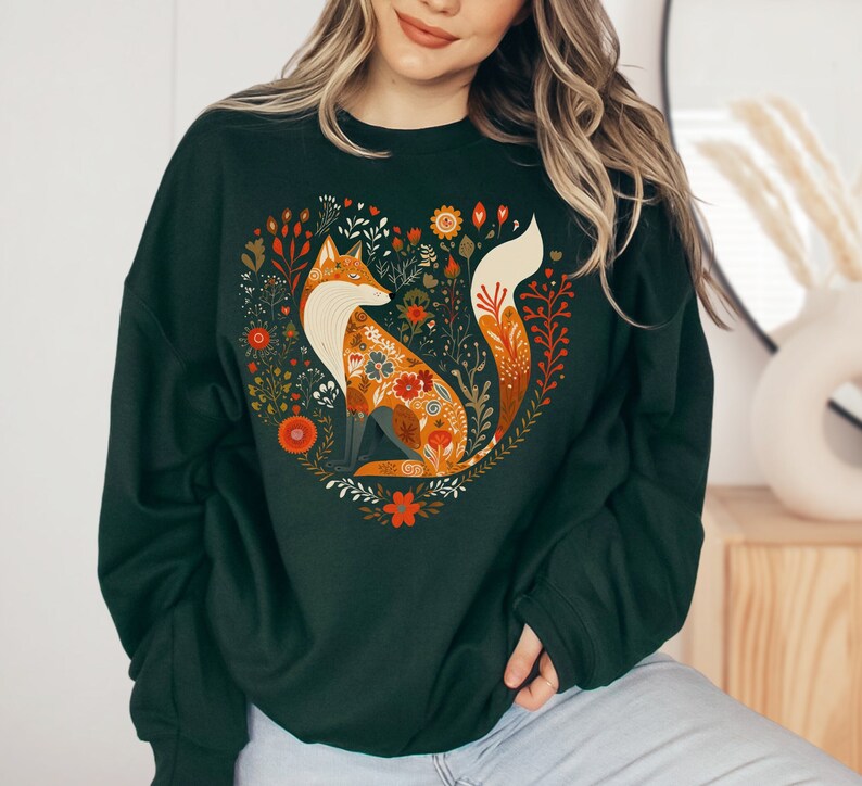 May include: A dark green sweatshirt featuring a graphic print of a fox surrounded by flowers. The fox is orange and white with a long, bushy tail.