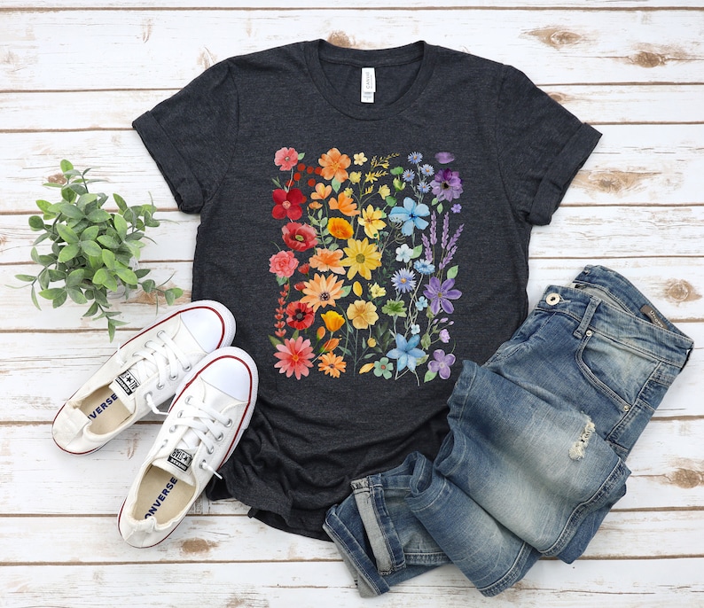 Puede incluir: Una camiseta gris oscuro jaspeada con un estampado floral arco&iacute;ris. Las flores son en tonos de rojo, naranja, amarillo, verde, azul y morado. La camiseta es de corte holgado y tiene cuello redondo.