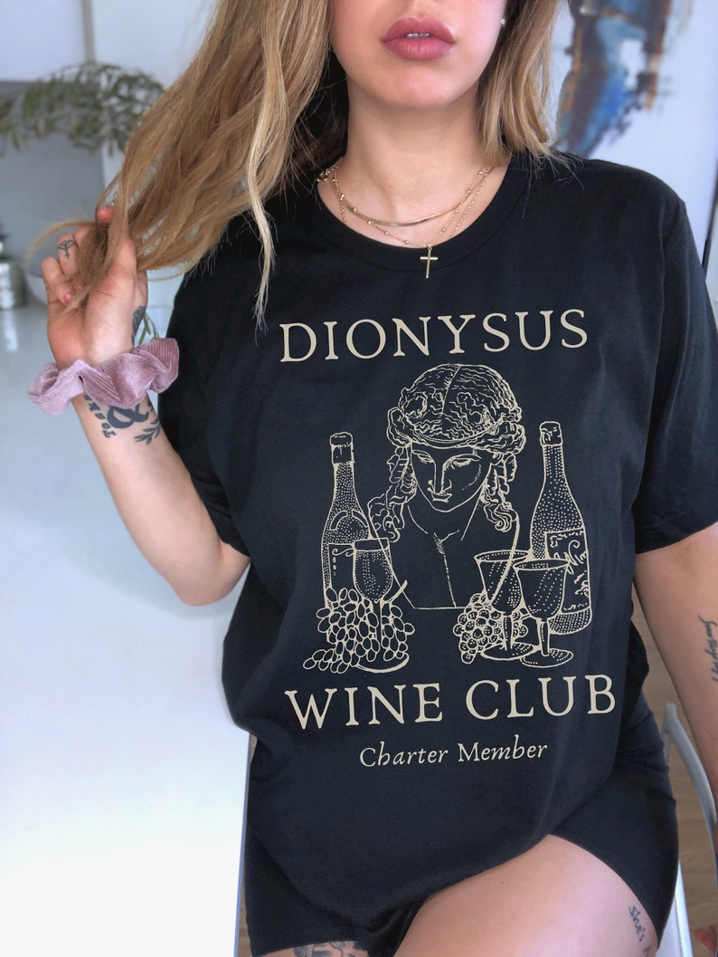 May include: Black t-shirt with a gold graphic of Dionysus, a Greek god, holding a wine glass and grapes. The text "Dionysus Wine Club Charter Member" is printed below the graphic.