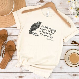 May include: A cream coloured t-shirt with a black raven illustration and a quote from Edgar Allan Poe that reads "An idle longing night and day to dream my very life away".