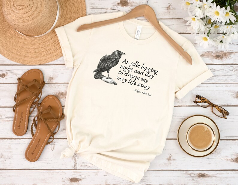 May include: A cream coloured t-shirt with a black raven illustration and a quote from Edgar Allan Poe that reads "An idle longing night and day to dream my very life away".