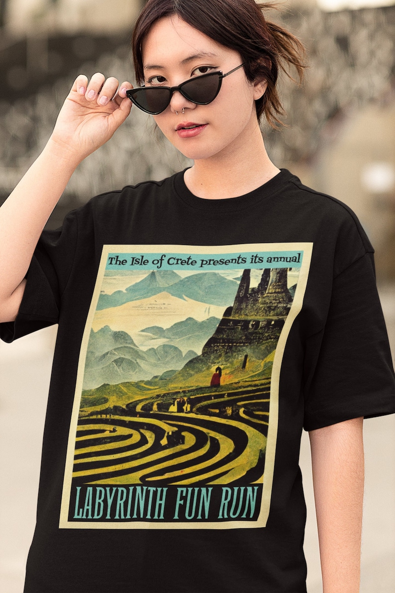 以下が含まれることがあります： 背景に山と城が描かれた迷路のヴィンテージスタイルのグラフィックがプリントされた黒いTシャツ。グラフィックには「The Isle of Crete presents its annual Labyrinth Fun Run」というテキストがプリントされています。