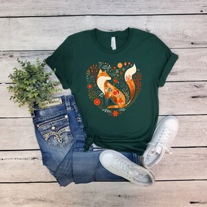 May include: A dark green t-shirt with a graphic of a fox surrounded by flowers in a heart shape. The fox is orange and white with a floral pattern.