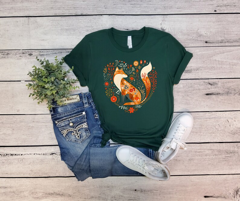 May include: A dark green t-shirt with a graphic of a fox surrounded by flowers in a heart shape. The fox is orange and white with a floral pattern.