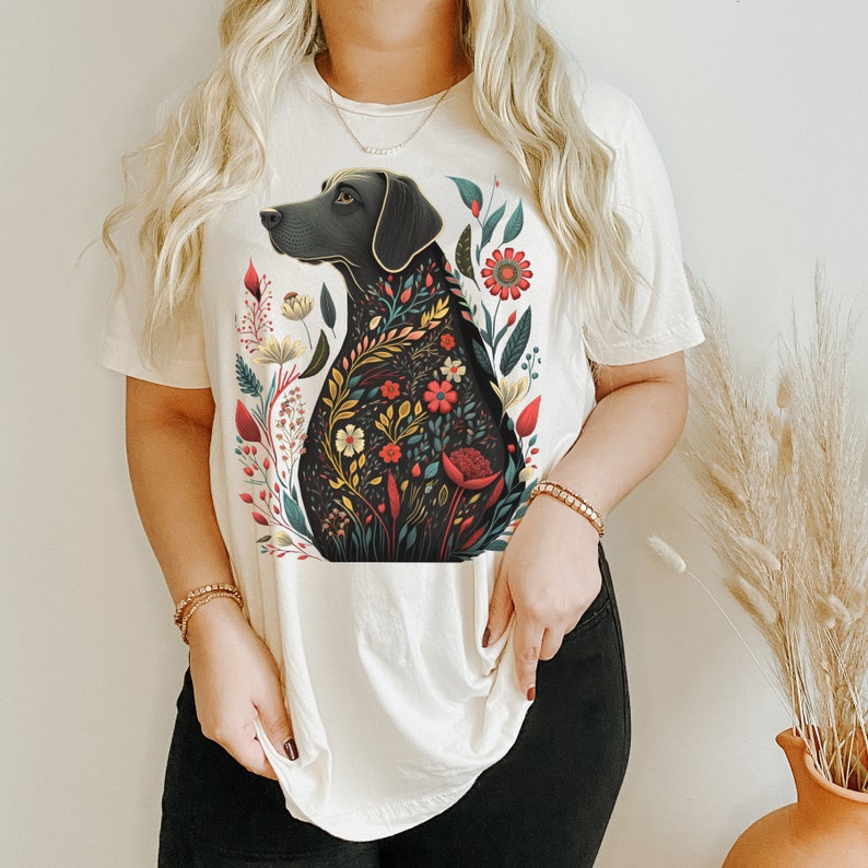 May include: A white t-shirt with a black dog silhouette design. The dog is surrounded by colorful flowers and leaves. The design is a floral pattern.