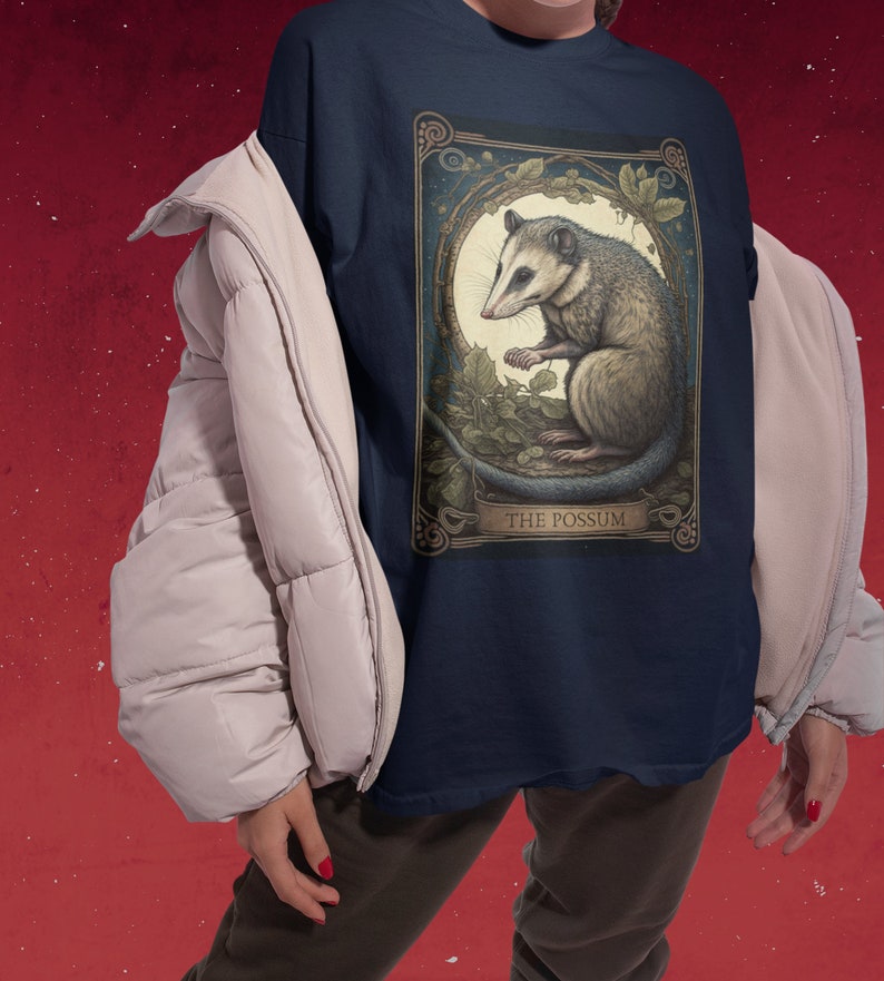 May include: A navy blue t-shirt with a vintage-style illustration of a possum. The illustration is surrounded by a gold frame and has the text "THE POSSUM" at the bottom.