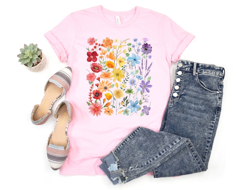 Puede incluir: Una camiseta rosa con estampado floral arco&iacute;ris. La camiseta se combina con jeans azules y pisos estampados.