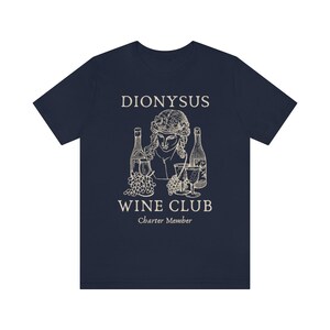 May include: Navy blue t-shirt with a white graphic of a bust of Dionysus with grapes and wine bottles. The text "Dionysus Wine Club Charter Member" is printed below the graphic.