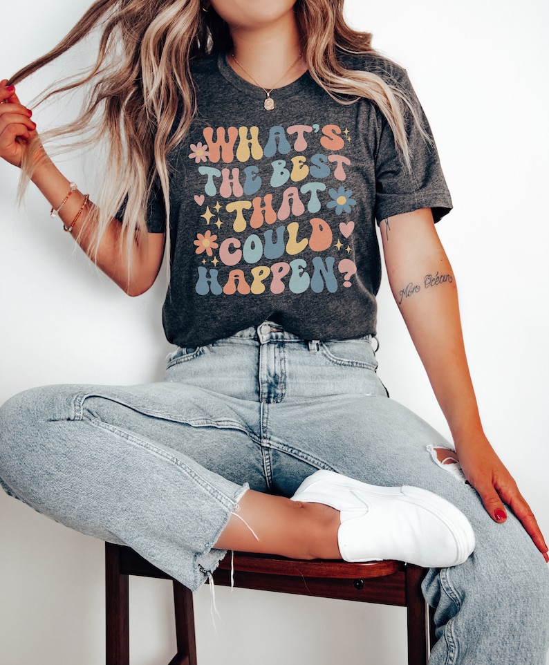 May include: A gray t-shirt with a retro-style graphic that reads "What's the best that could happen?" The graphic is in rainbow colors with flowers and hearts.