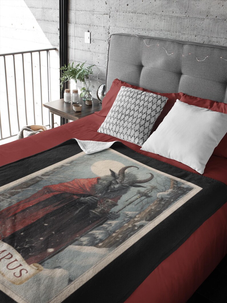 May include: A black and white throw blanket with a vintage illustration of a horned figure in a red cloak holding a cup. The illustration is set against a snowy background with a full moon. The text "Krampus" is visible at the bottom of the illustration.