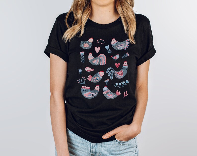 K&ouml;nnte beinhalten: Schwarzes T-Shirt mit einem bunten Muster aus stilisierten V&ouml;geln und Blumen. Die V&ouml;gel sind rosa, blau und grau mit filigranen Details.