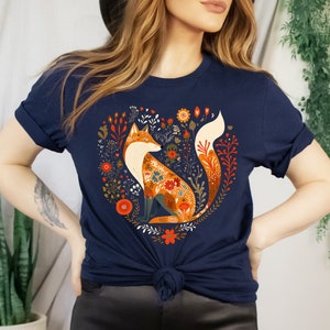 May include: A navy blue t-shirt with a graphic of a fox surrounded by flowers in a heart shape. The fox is orange and white with floral patterns on its fur.