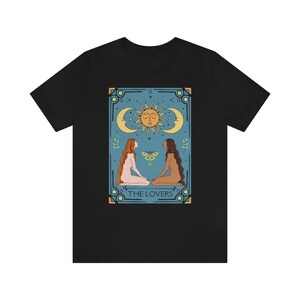 May include: Black t-shirt with a graphic of a tarot card depicting two figures facing each other, a sun and moon above them, and the text "THE LOVERS".