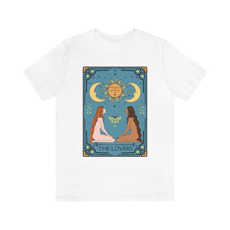 May include: White t-shirt with a graphic of the Lovers tarot card. The card features two women facing each other, a sun and moon, and the text "THE LOVERS".