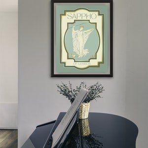 Op de afbeelding: Een ingelijste kunstdruk met de naam "Sappho" en een illustratie van een vrouw in gewaden. Het kunstwerk gebruikt een gedempte kleurenpalet van groen, cr&egrave;me en goud. Een zwarte vleugel staat op de voorgrond, met een vaas bloemen.